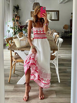 Woman wearing a white and pink embroidered maxi dress, lifting the hem to show the details.