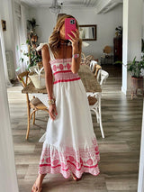 Woman wearing a white and pink embroidered maxi dress, standing in a dining room.