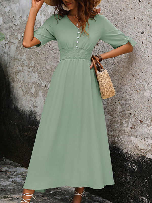 Woman wearing a sage green A-line maxi dress with a smocked waist and tie sleeves, holding a straw bag.