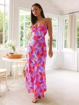 Front view of a woman in a purple and orange floral print maxi dress with spaghetti straps and a ruched bust, looking at the camera.