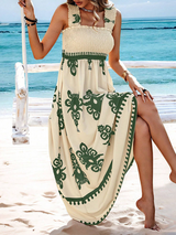 Woman sitting on a swing on a beach wearing a cream and green floral print maxi dress with smocked bodice and square neckline.