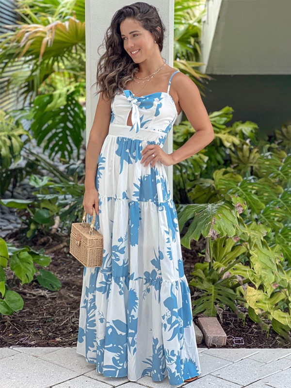 Woman in a white and blue floral print maxi dress with a tie-front bodice and tiered skirt, standing outdoors and smiling.