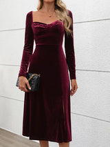 Woman in a wine-colored velvet midi dress with a sweetheart neckline and long sleeves, holding a black clutch.