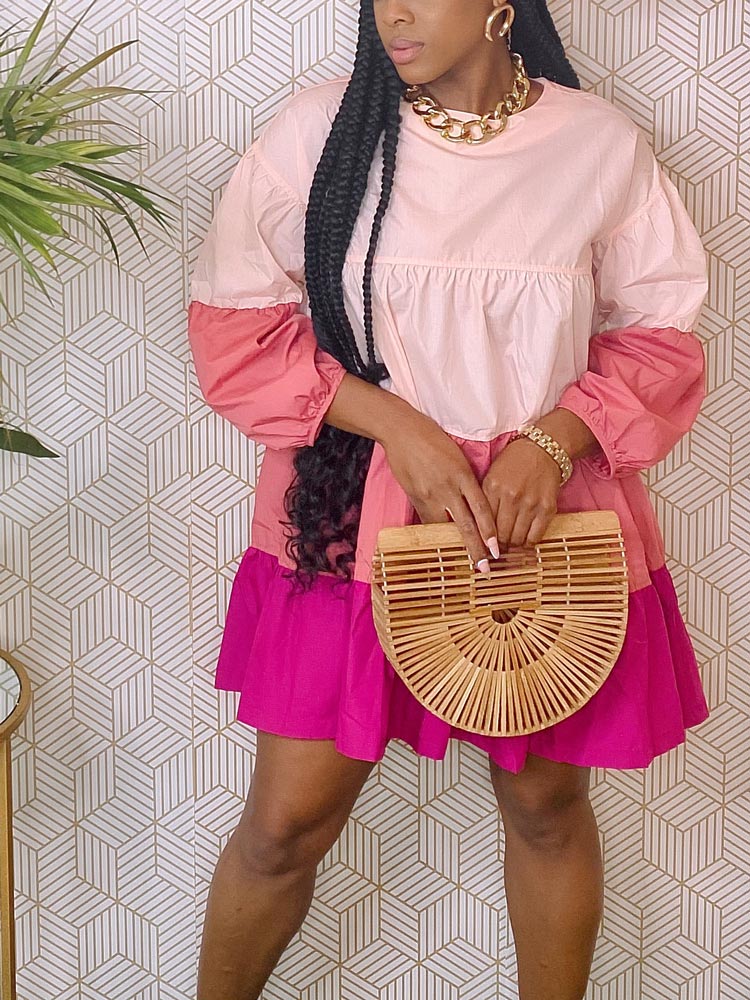 Close-up of a woman wearing a pink and purple tiered dress, gold chain necklace, gold bracelet, and bamboo handbag.