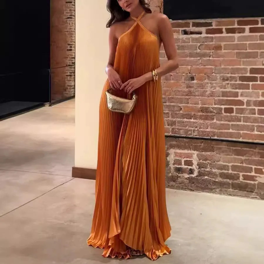 woman in orange pleated halter maxi dress with gold clutch, standing