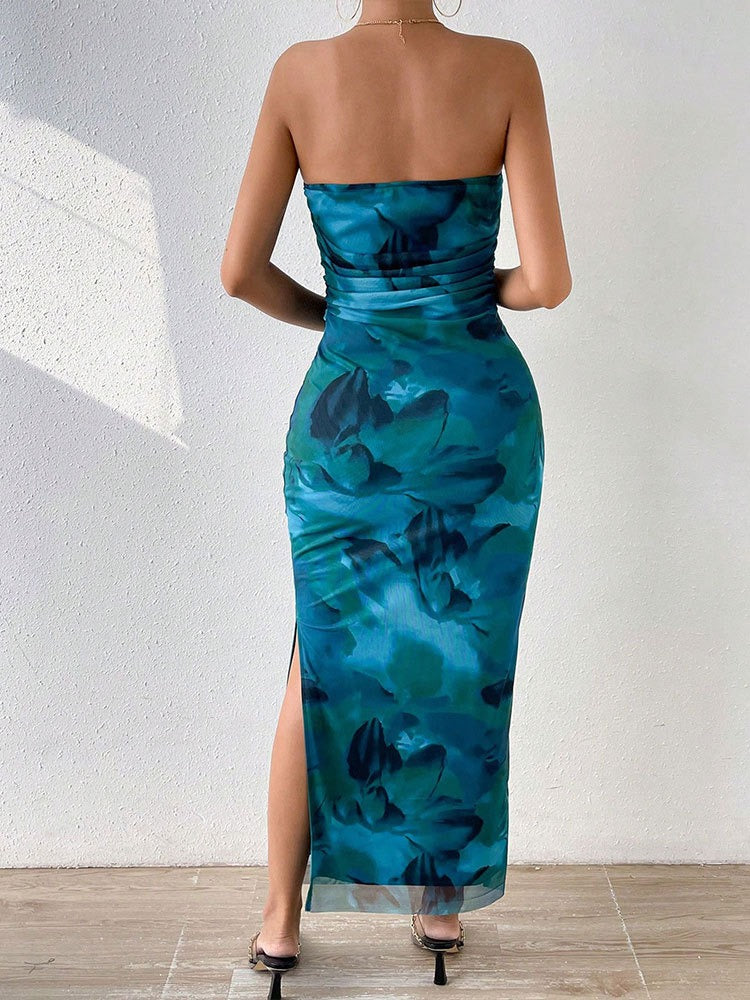 Rear view of a woman wearing a strapless blue and green abstract floral print maxi dress with a high slit.