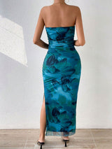 Rear view of a woman wearing a strapless blue and green abstract floral print maxi dress with a high slit.