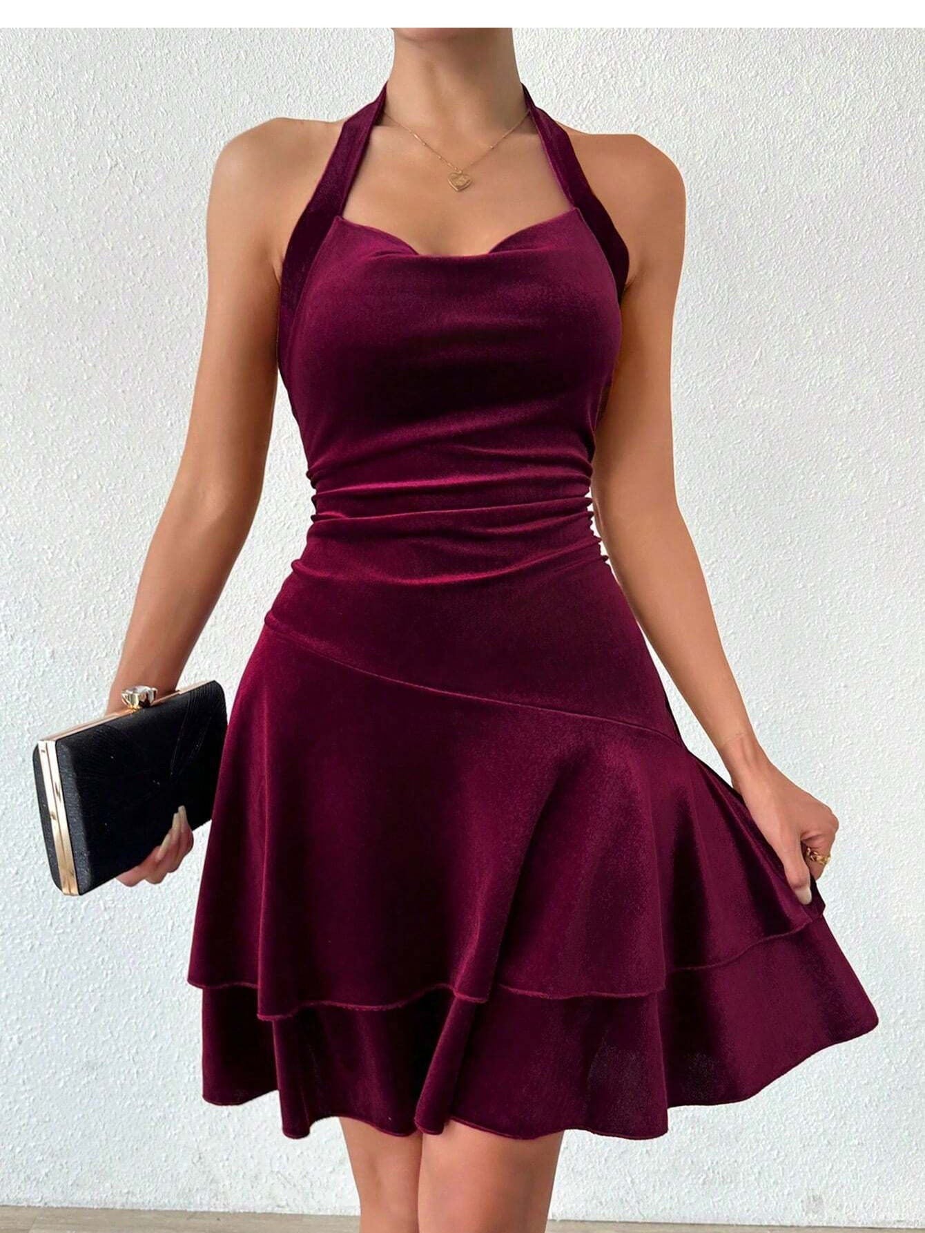 Woman holding a black clutch while wearing a maroon velvet halter dress