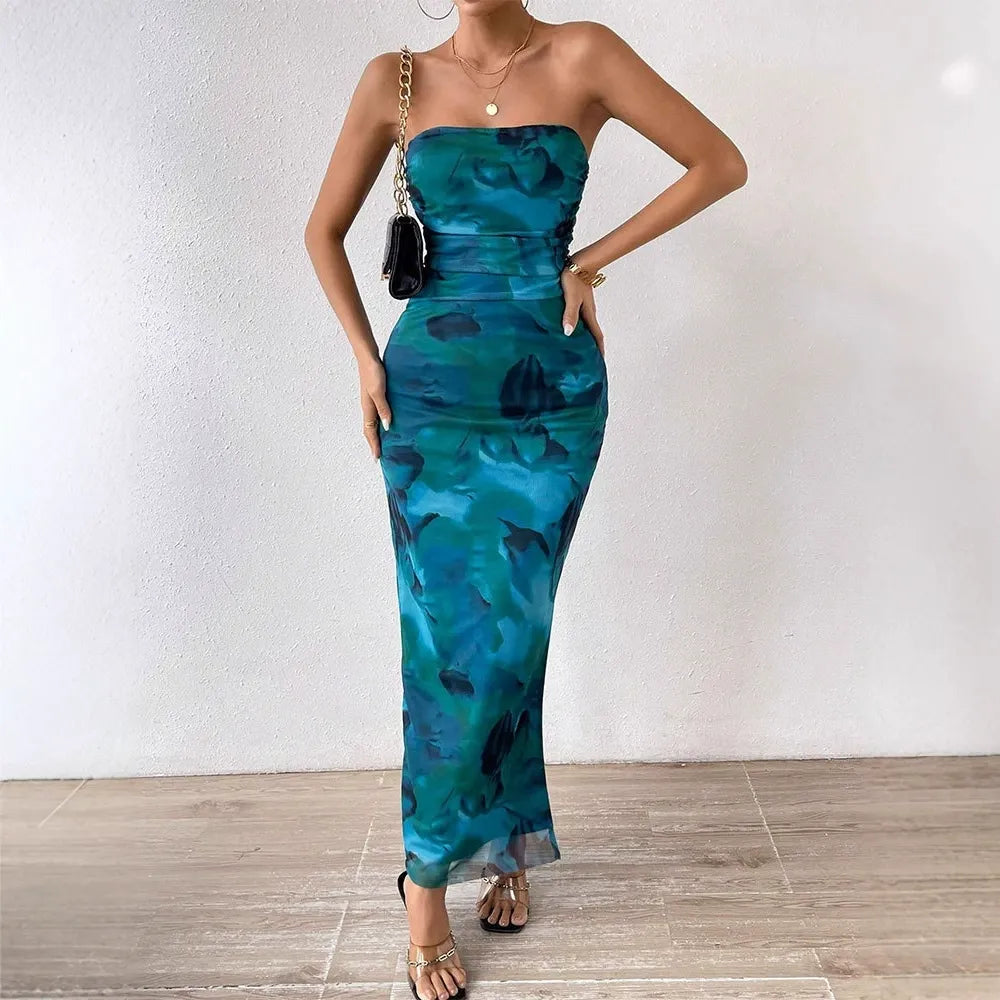 Woman wearing a strapless blue and green abstract floral print maxi dress with a high slit, gold heeled sandals, and a black clutch.