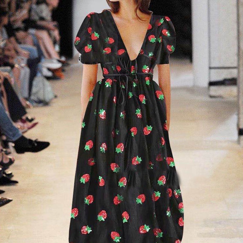 Woman wearing a black midi dress with a strawberry print and puff sleeves on a runway.