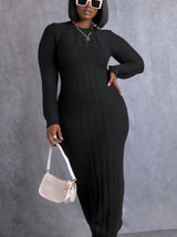 Woman wearing a long black cable knit dress with long sleeves and a mock neck, holding a white handbag.