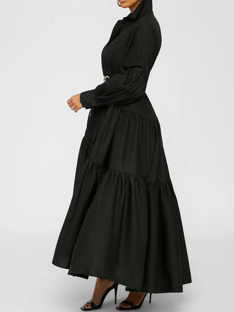 Side profile of a woman wearing a black tiered maxi dress with a collared neckline and a wide black belt.