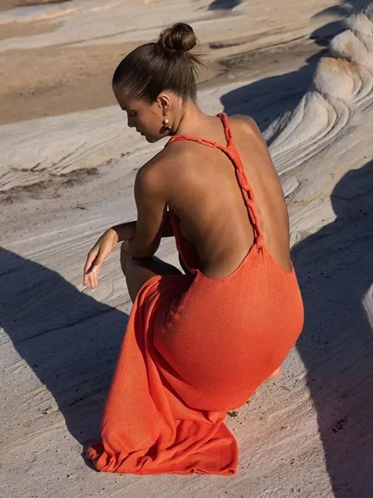 Woman wearing an orange knit maxi dress with braided straps and an open back, posing outdoors on rocks.