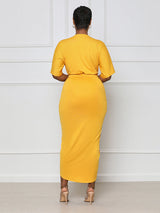 Back view of a woman wearing a yellow V-neck, short-sleeve, ruched, draped midi dress with a tulip hem.