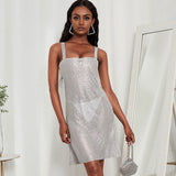 Woman wearing a silver sparkling mini dress with a square neckline and thin straps, holding a small silver handbag.