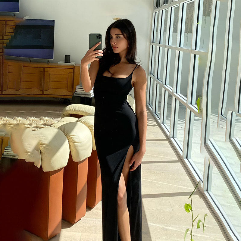 Woman wearing a black sleeveless maxi dress with a high slit, taking a mirror selfie in a sunlit room with large windows and modern furniture.