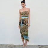 Full-body shot of a model wearing a strapless, full-length dress with a landscape print, facing the camera.