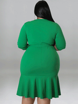 Back view of a plus-size model wearing a green wrap dress with a ruffle hem and three-quarter sleeves.
