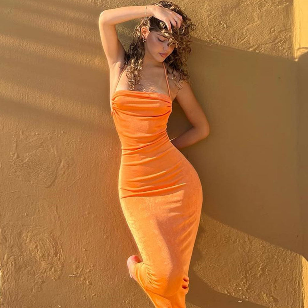 Woman in an orange halter neck maxi dress with ruched detailing standing against a textured wall.