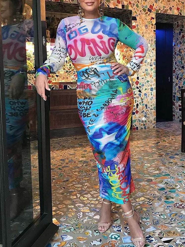 Full-length view of a woman in a colorful graffiti-print dress, leaning against a doorway.
