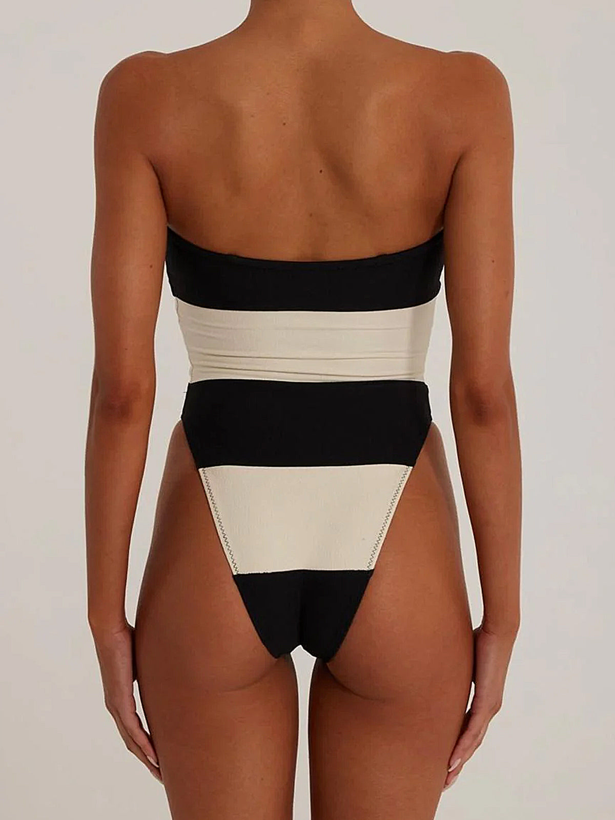 Back view of a woman wearing a black and white striped strapless one-piece swimsuit with a high-cut leg.