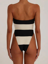Back view of a woman wearing a black and white striped strapless one-piece swimsuit with a high-cut leg.