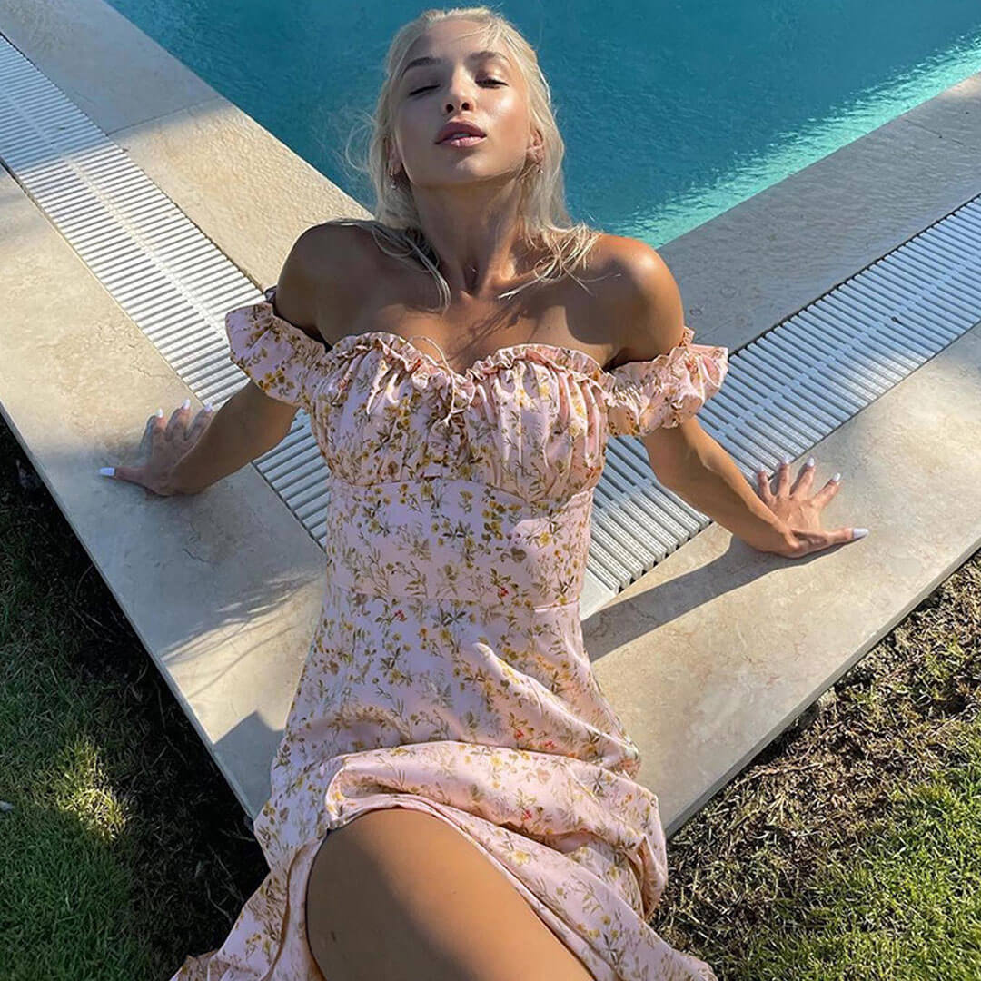 Woman in a pink floral off-the-shoulder maxi dress with a high slit posing by a swimming pool.