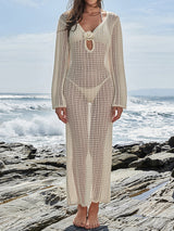 Woman wearing a cream crochet maxi dress over a cream bikini, standing on rocks by the ocean.