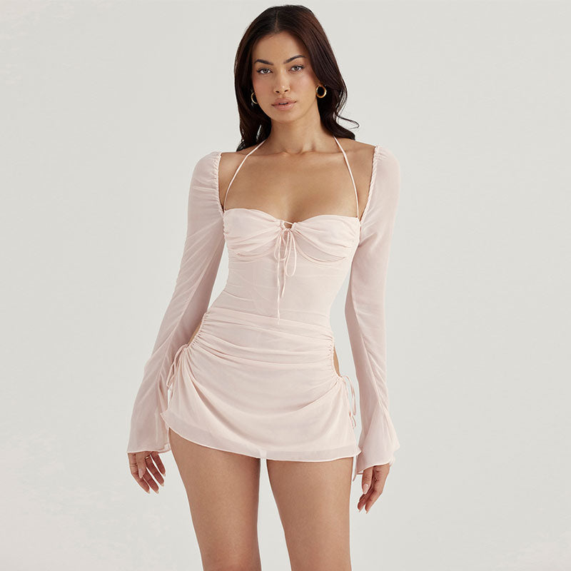 Woman wearing a light pink sheer chiffon mini dress with long sleeves and ruched detailing.