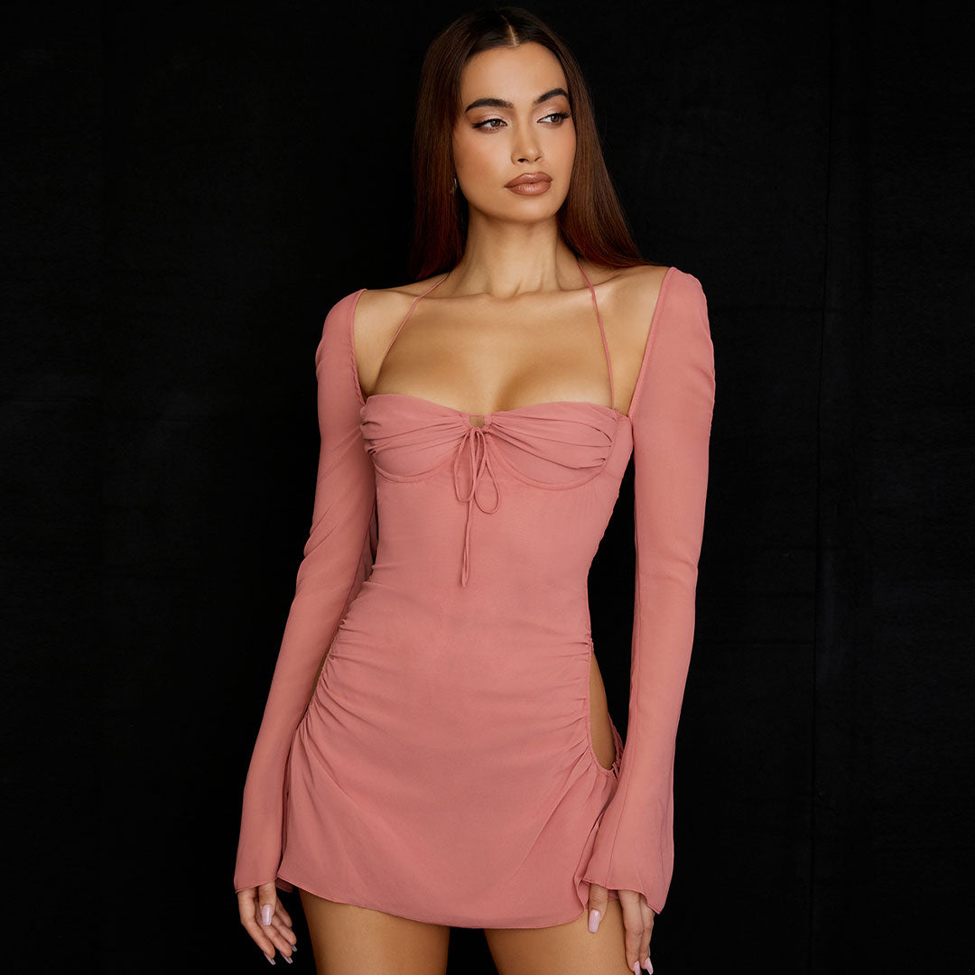 Model wearing a pink ruched mini dress with cut-out sides and long bell sleeves, angled side view.