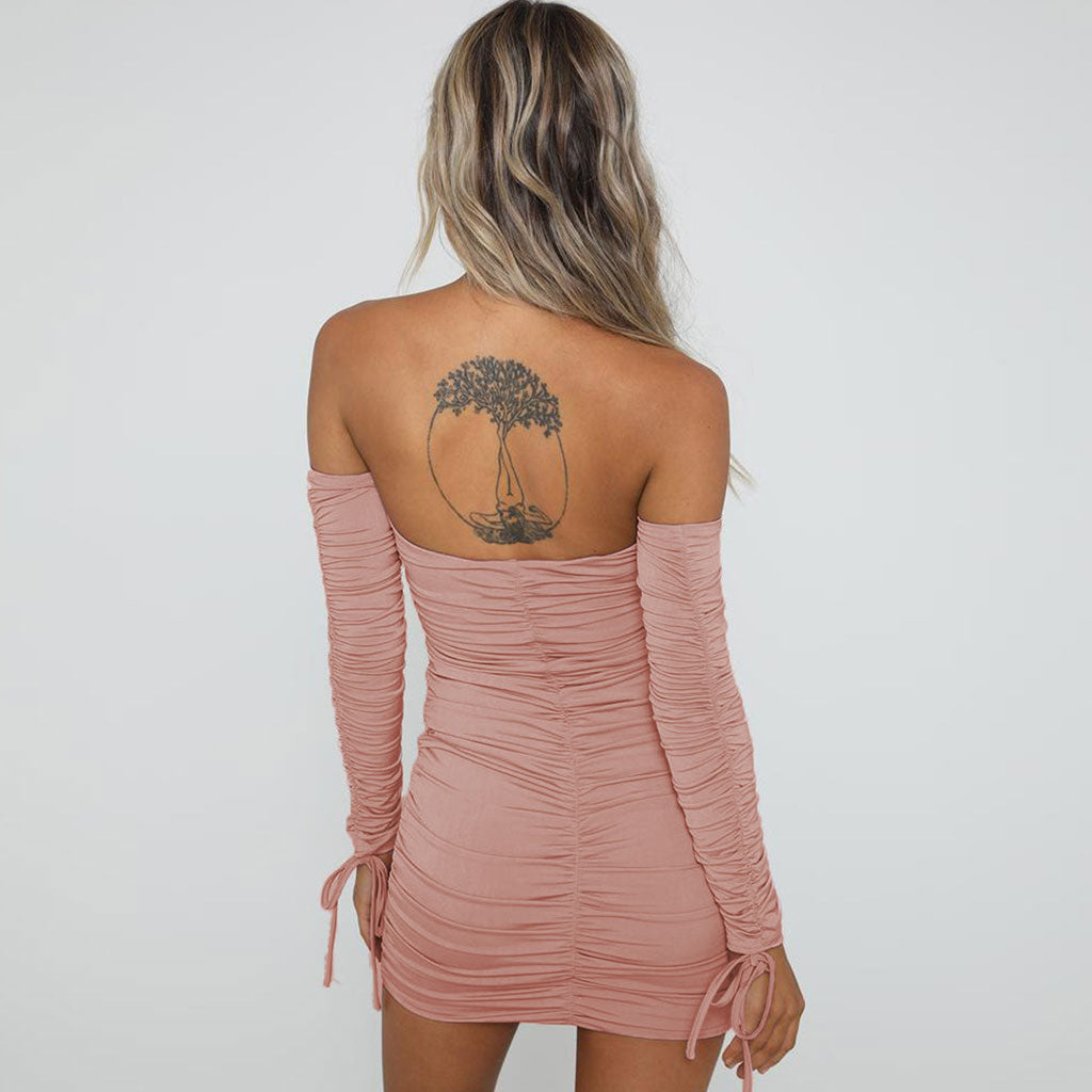 Back view of a woman in a pink off-the-shoulder ruched mini dress with long sleeves and tie cuffs