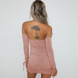 Back view of a woman wearing a pink off-the-shoulder long-sleeved ruched mini dress with a tie front and cutout.