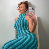 Woman with hair in a bun taking a selfie in a turquoise and blue striped crinkle knit halter maxi dress