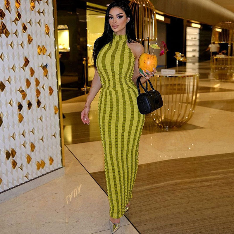 Woman wearing a lime green striped sleeveless maxi dress with a halter neckline, holding a coconut drink and a black handbag.