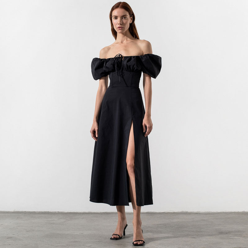 Woman wearing a black off-the-shoulder midi dress with puffed sleeves and a high slit, front view.