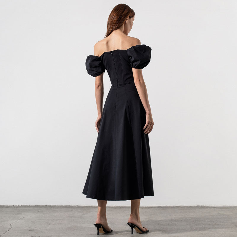 Woman wearing a black off-the-shoulder midi dress with puffed sleeves and a high slit, back view.