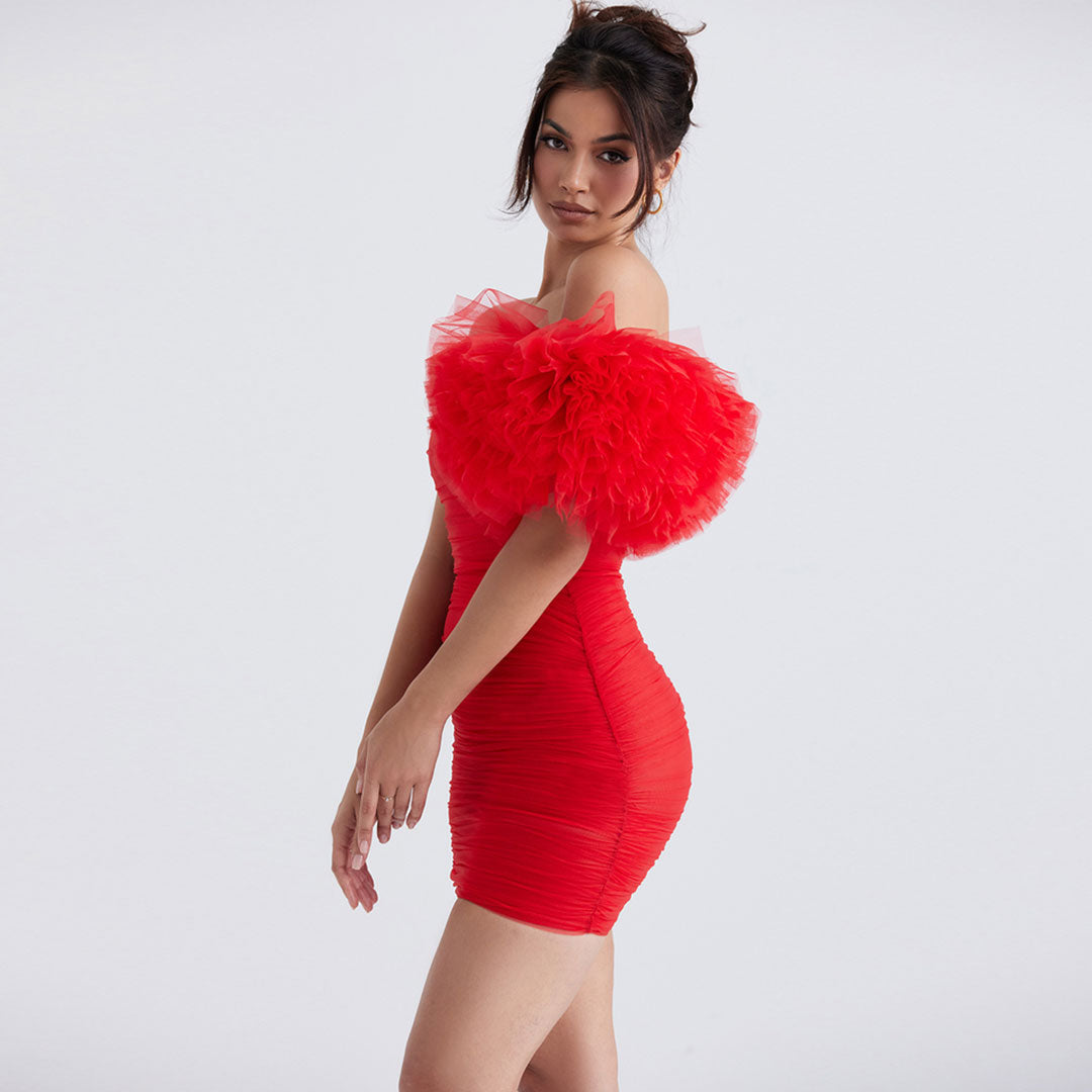 Side view of a woman in a red strapless ruched mini dress with a large ruffle sleeve