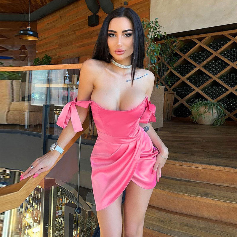 Woman wearing a pink off-the-shoulder satin dress with tie details and a ruched skirt.