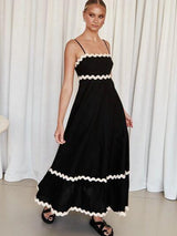 Woman wearing a black maxi dress with white scalloped trim and spaghetti straps.