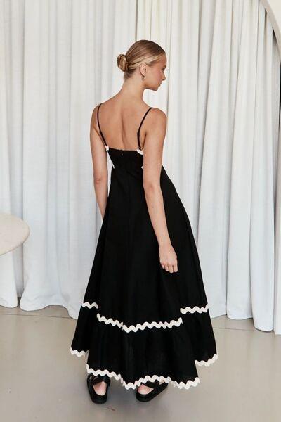 Rear view of a woman in a black maxi dress with white scalloped trim.