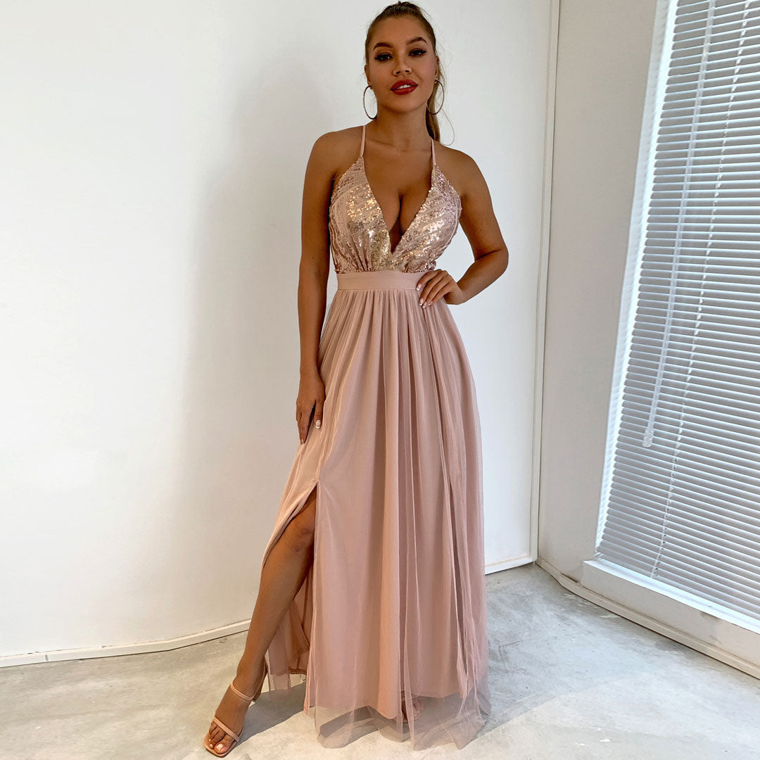 Full length shot of a woman wearing a blush pink formal dress with a sequined bodice and a high slit.