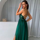 Woman in a green sequined and tulle maxi dress with a high slit, showing the back of the dress.