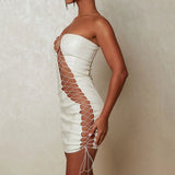 Side view of a woman in a white strapless faux leather mini dress with cut-out accents and lace-up details