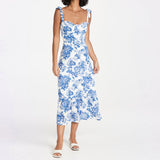 Woman wearing a white midi dress with a blue floral print and tie shoulder straps, standing front view.