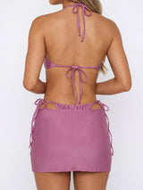 Back view of a woman wearing a mauve bikini set with a halter top and ruched mini skirt.