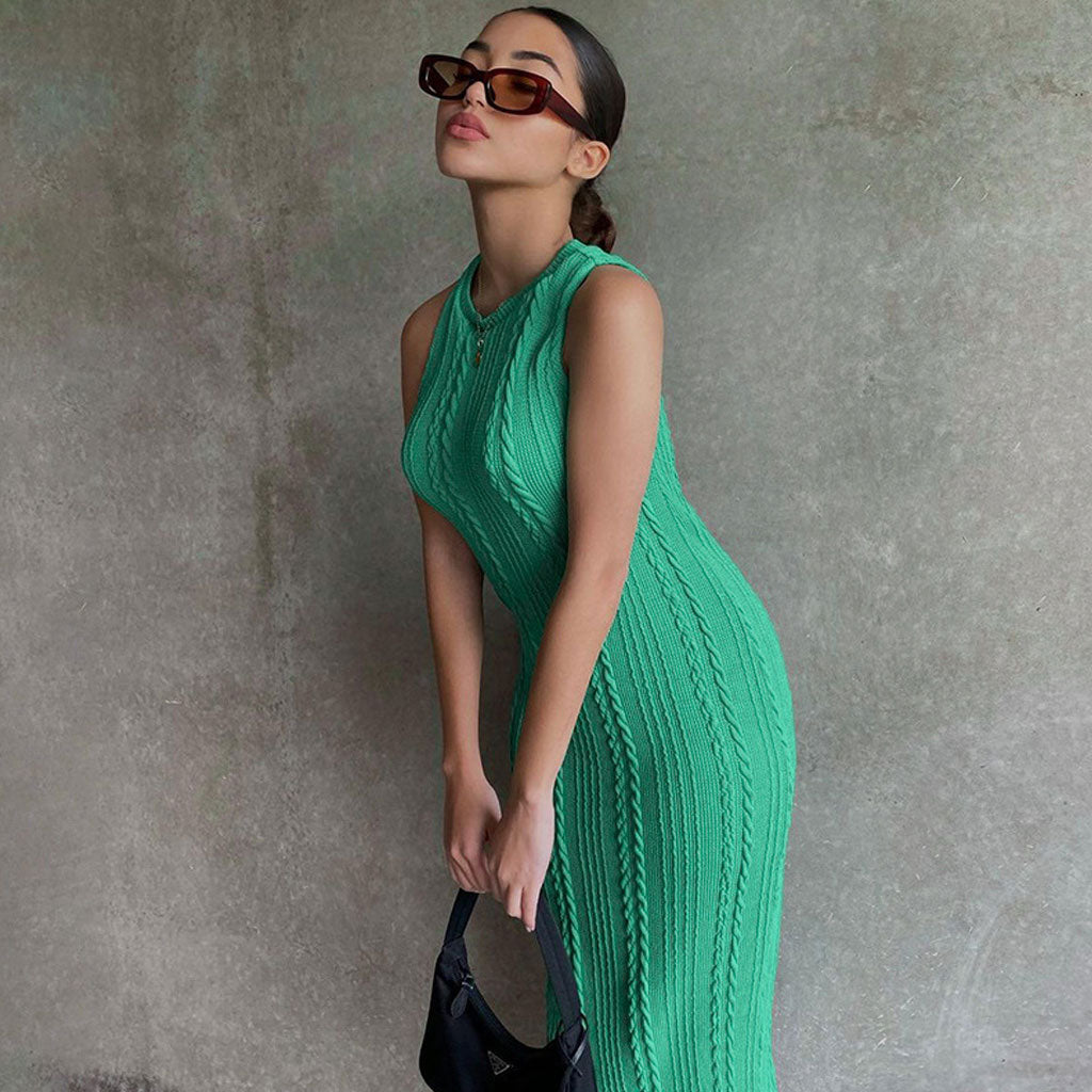 Woman posing in a green sleeveless midi dress with a ribbed texture and cable knit detailing, holding a black handbag.