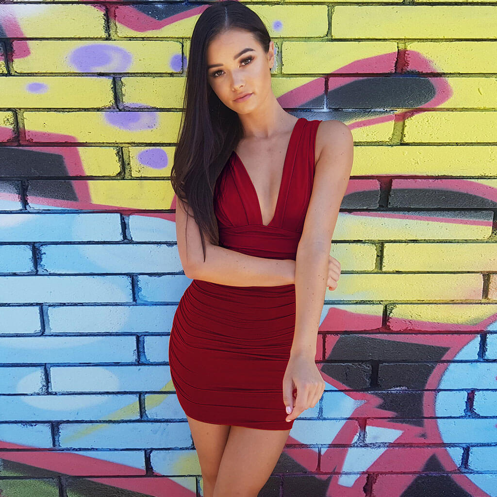 Woman wearing a red ruched bodycon dress with a deep V-neckline, standing in front of a graffiti wall.