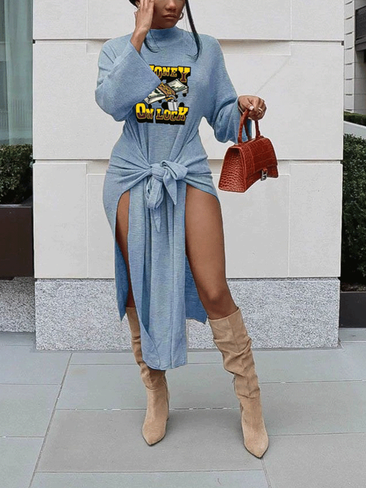 Woman wearing a light blue long-sleeve mock neck dress with a tie waist and high slits, featuring a graphic print of money. She is also wearing tan knee-high boots and carrying a red textured handbag.