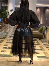 Rear view of a woman wearing a black shirt dress with a sheer black tiered tulle skirt overlay and denim shorts, with braided hair.