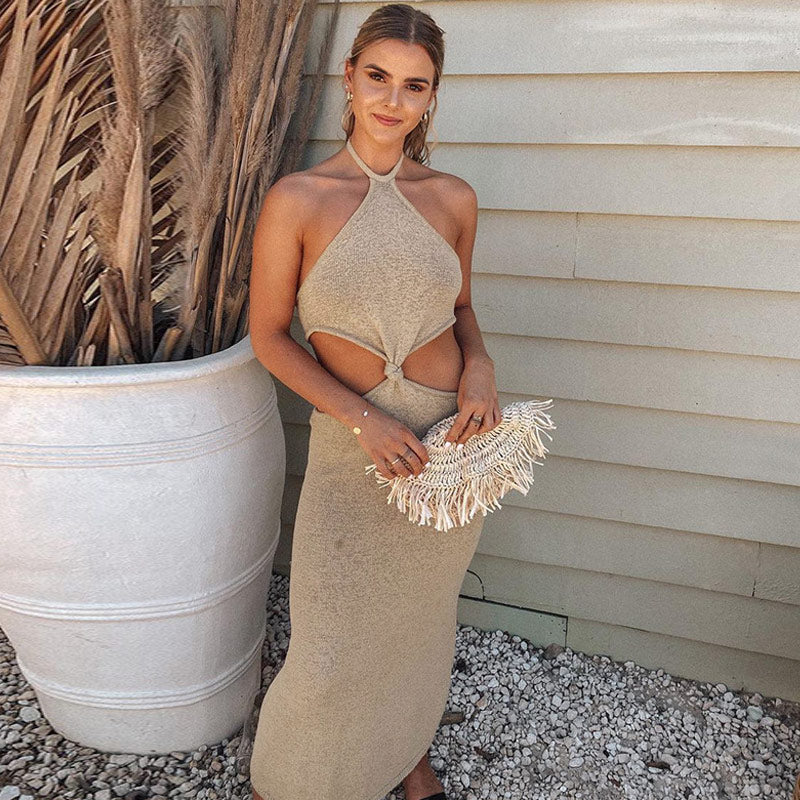 Woman wearing a beige knit midi dress with cut-out detailing and a halter neckline, posing with a clutch.